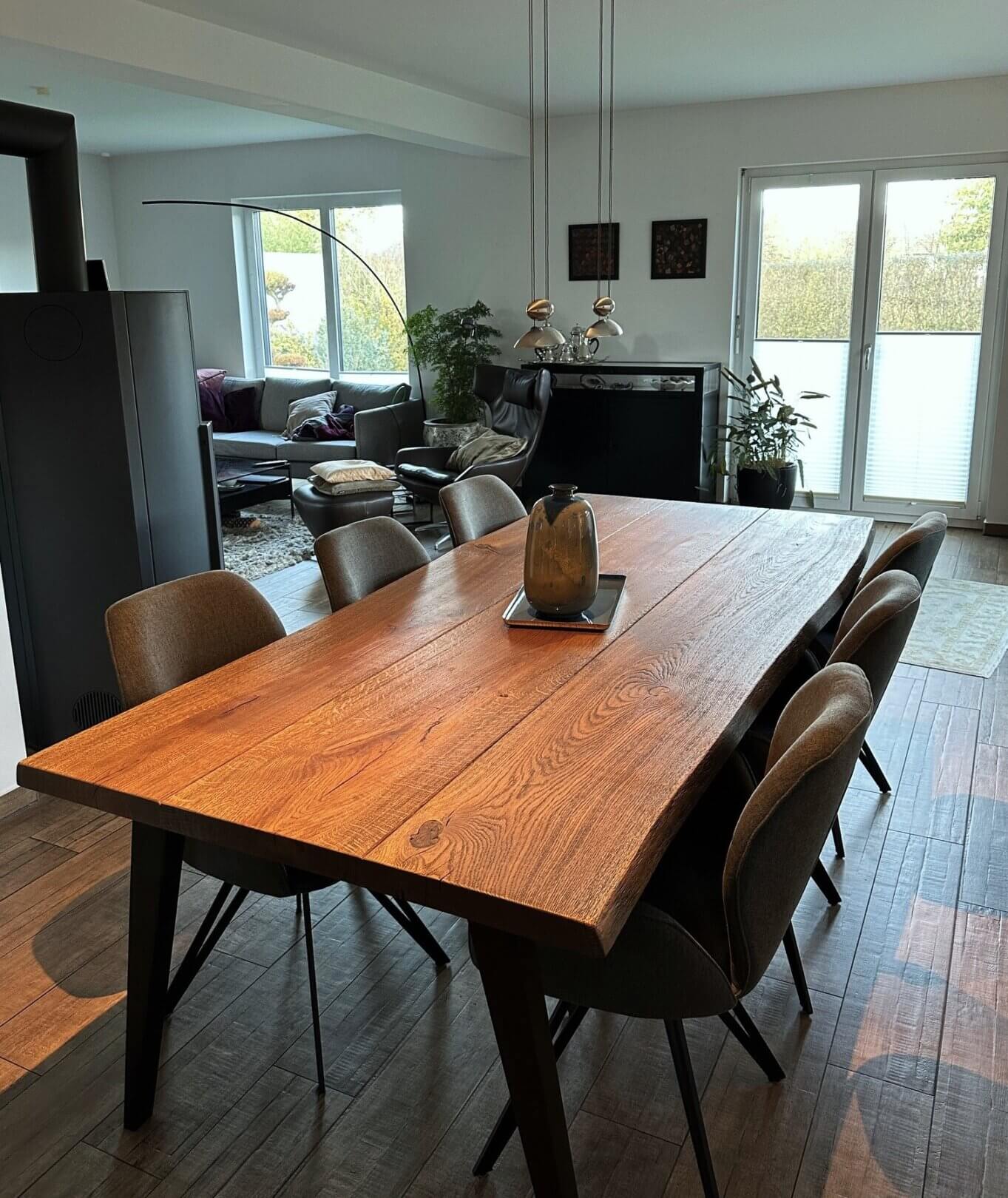Rustikaler esstisch aus eiche mit naturgewachsener baumkante, drei bohlen und v-fuge, sechs olivgrüne stühle mit schwarzen stahlbeinen, grüne tonvase.