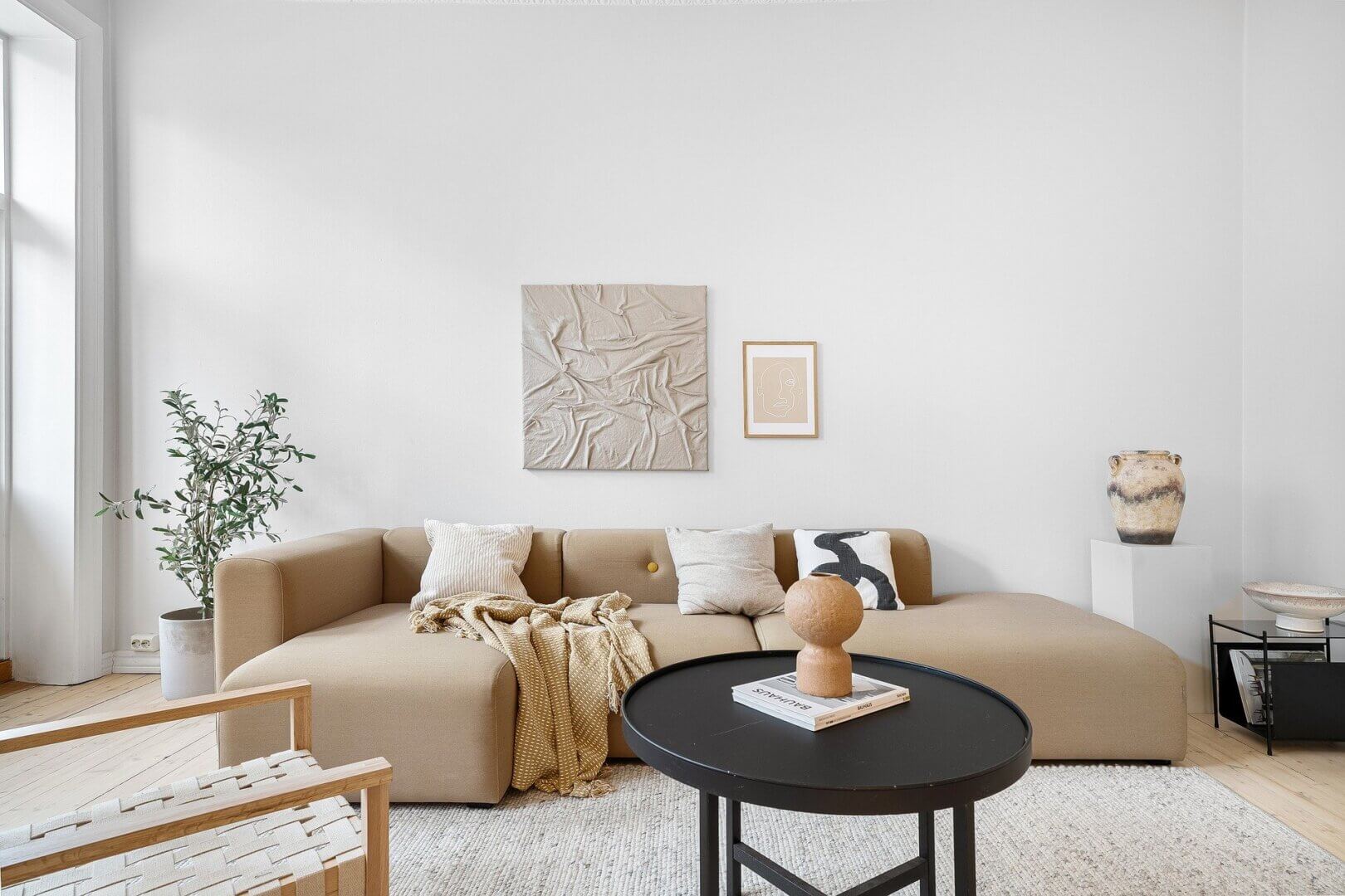 Wohnzimmer im modern-organic-stil mit beigem sofa, schwarzem tisch, keramikelementen und zimmerpflanze auf hellem holzboden.