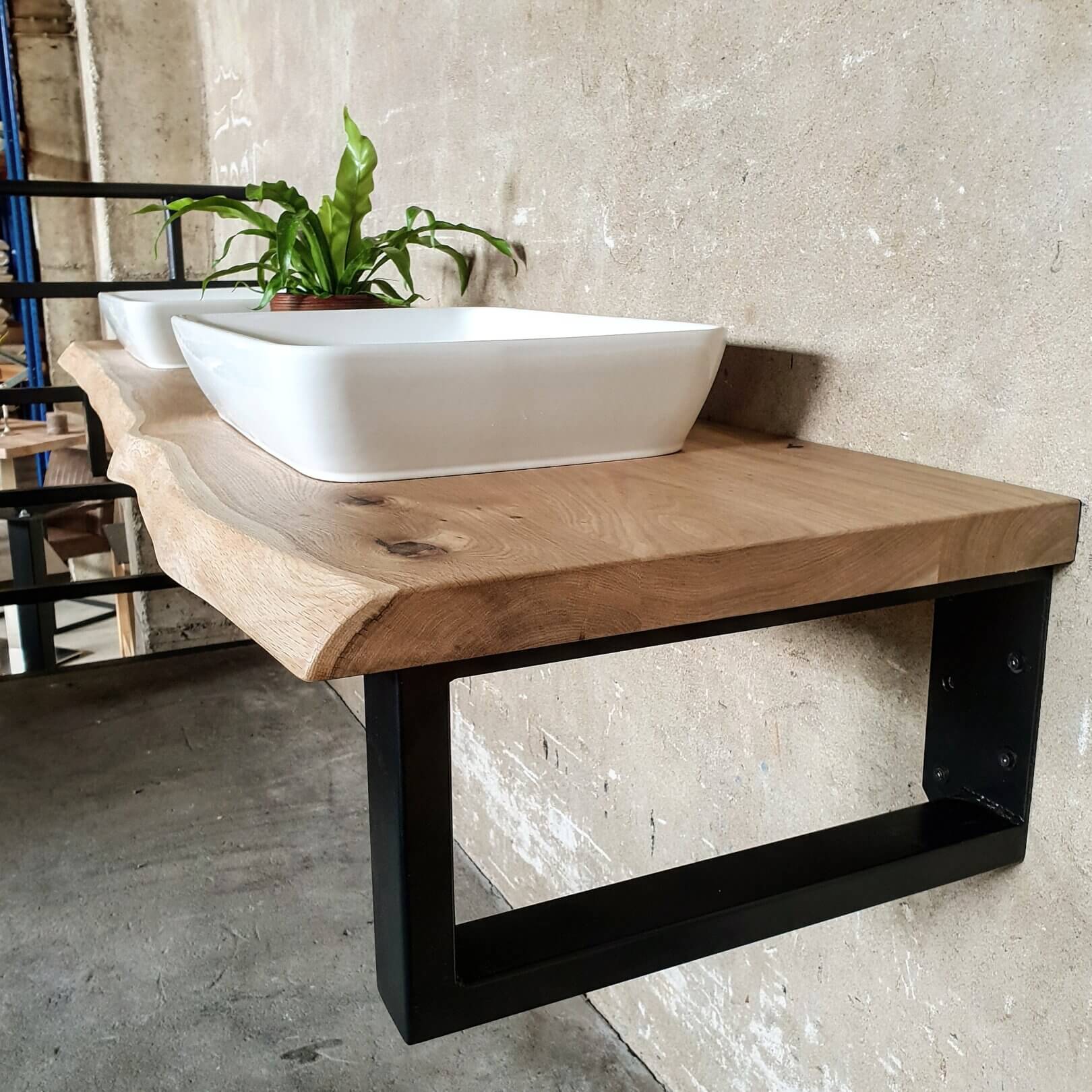 Eichen-waschtischplatte 40 mm dick mit geschwungener baumkante, zwei waschbecken, schwarzem trägerregal, grüner zimmerpflanze, betonwand und betonboden im modernen organischen einrichtungsstil
