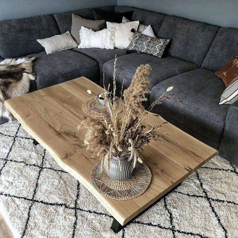 Baumkante couchtisch vor grauem sofa, dekoriert mit trockenblumen