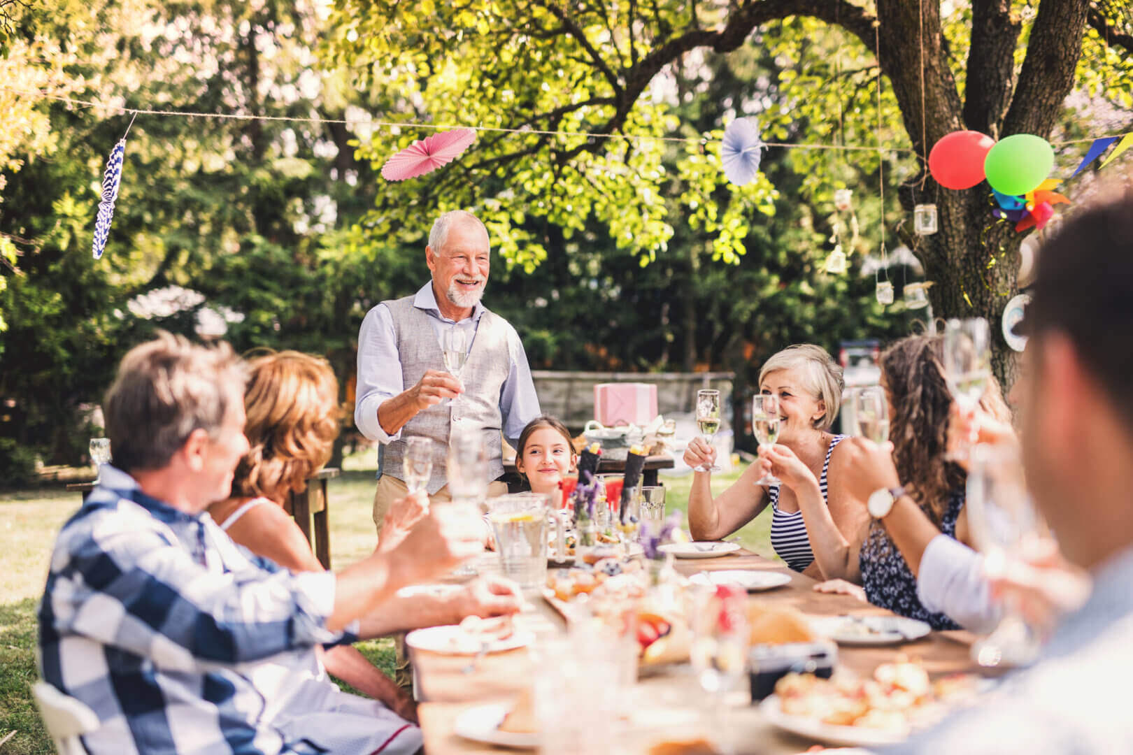 Familienfeier im garten: menschen stoßen an einem outdoortisch aus holz auf den frühling an.