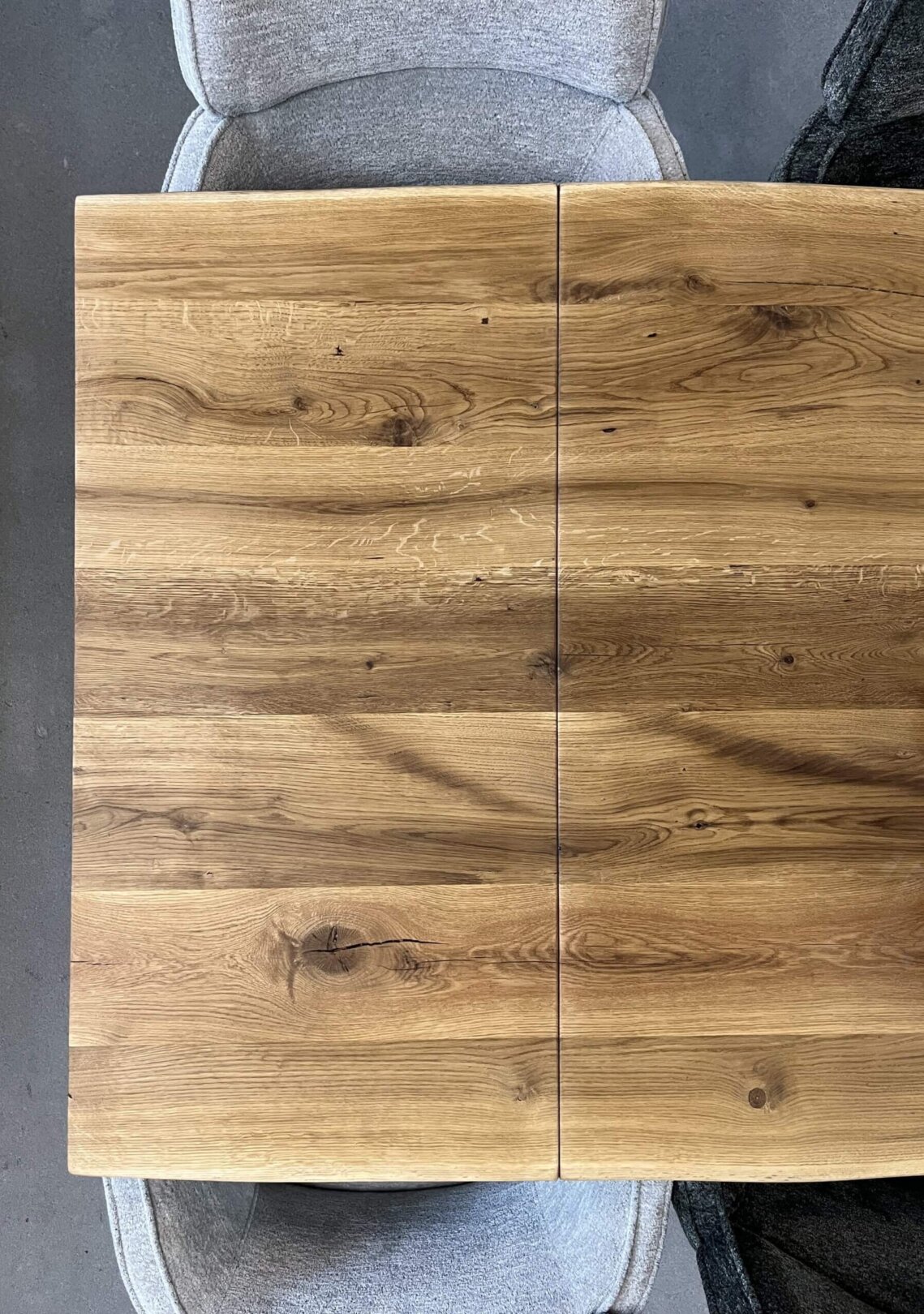 Draufsicht auf massivholztisch mit nahtloser verbindung der tischplatte und ansteckplatte, die natürliche holzmaserung und sichtbare äste harmonisch fortsetzt.