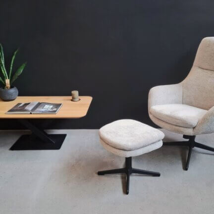 Loungechair mit hocker in heller stofffarbe vor dunkler wand mit couchtisch.