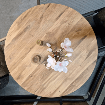 Runde eichentischplatte mit lebendiger maserung dekoriert mit weiß-rose blumen und grünen kerzen, umstellt von zwei schwingstühlen