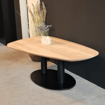 Organisch geformter couchtisch aus eiche in kieselform mit schwarzem mittelfuß, dekoriert mit vase und trockenblumen.